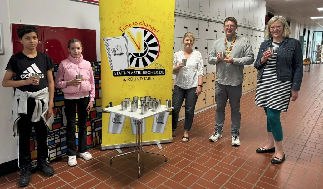 Übergabe von Edelstahlbechern an eine Schule vor dem Roll-up „statt-plastik-becher.de by Round Table"